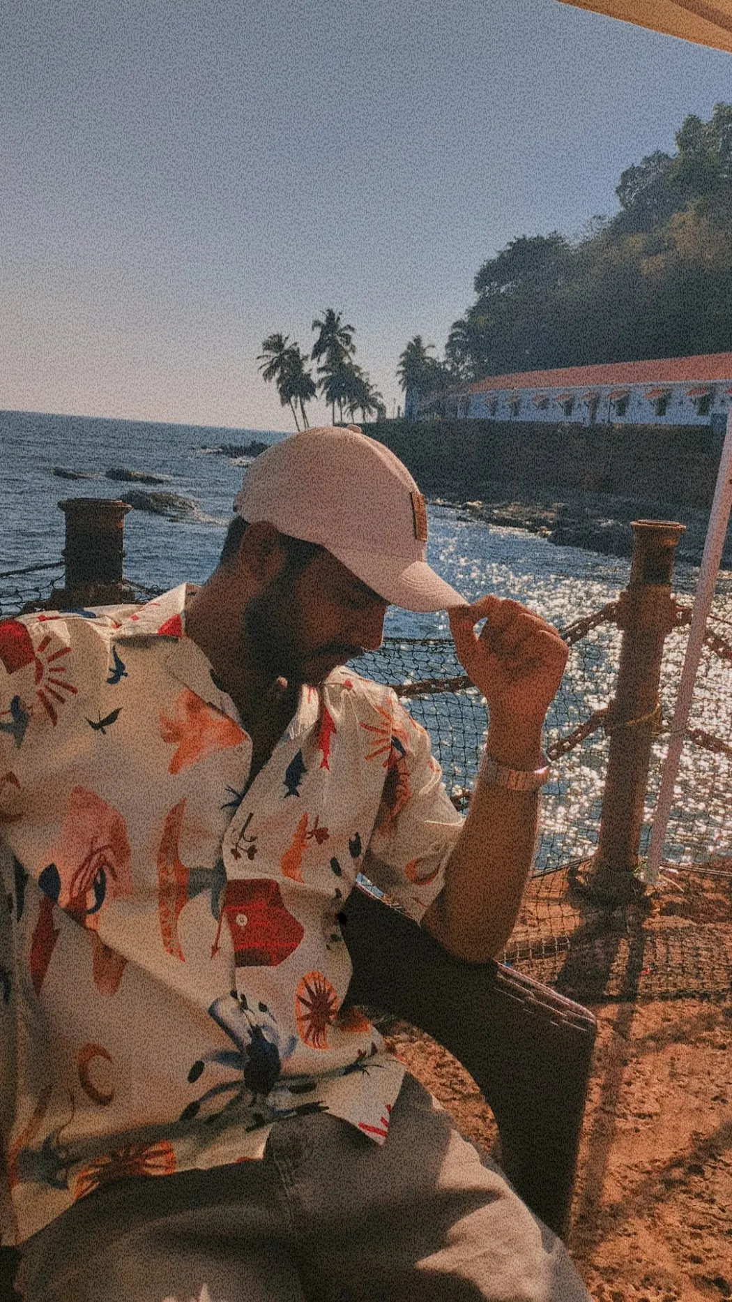 Man in a cap and printed shirt sitting by the sea in Goa