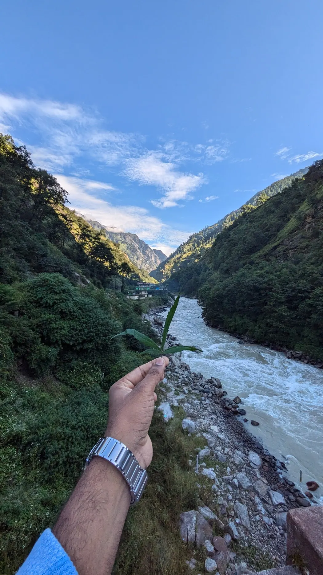 Hand reaching out over a rushing river in a green mountain valley